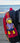 Red bagpack with a  W.E.Kiwi mini plushie on a blurred New Zealand beach background